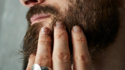 Gros plan sur un homme qui passe la main dans sa barbe, au niveau de la joue