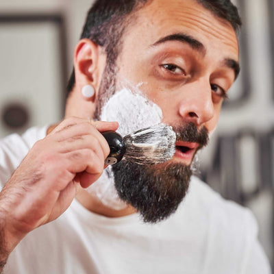 Homme barbu appliquant la mousse à raser sur sa joue avec le blaireau de barbier Monsieur BARBIER LE BLAIREAU, poils souples et répartition homogène.