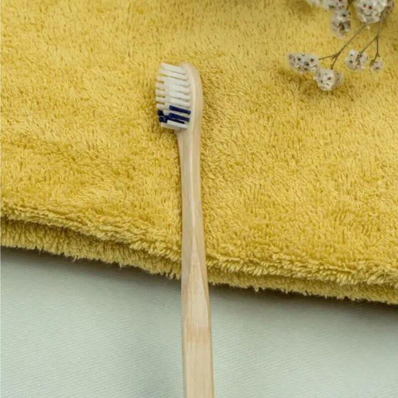 Brosse à dents epimeni en bois à poils bleus, posée sur une serviette jaune