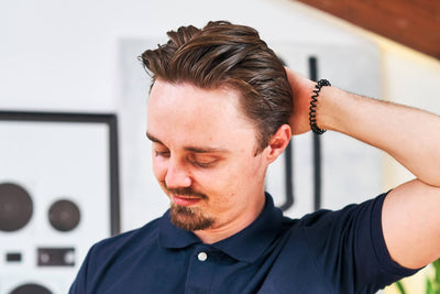 Homme en polo bleu marine passant la main dans ses cheveux coiffés en arrière à la cire, mèches structurées et brillantes