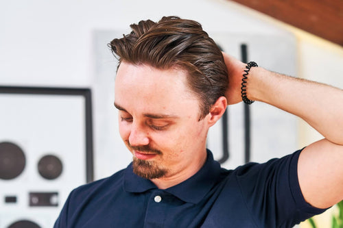 Homme en polo bleu marine passant la main dans ses cheveux coiffés en arrière à la cire, mèches structurées et brillantes