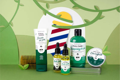 Gamme barbe et cheveux Monsieur BARBIER dans un décor de papier vert : baume de soin, huiles sèches, shampoing FULL CARE, cire coiffante et peigne en bois