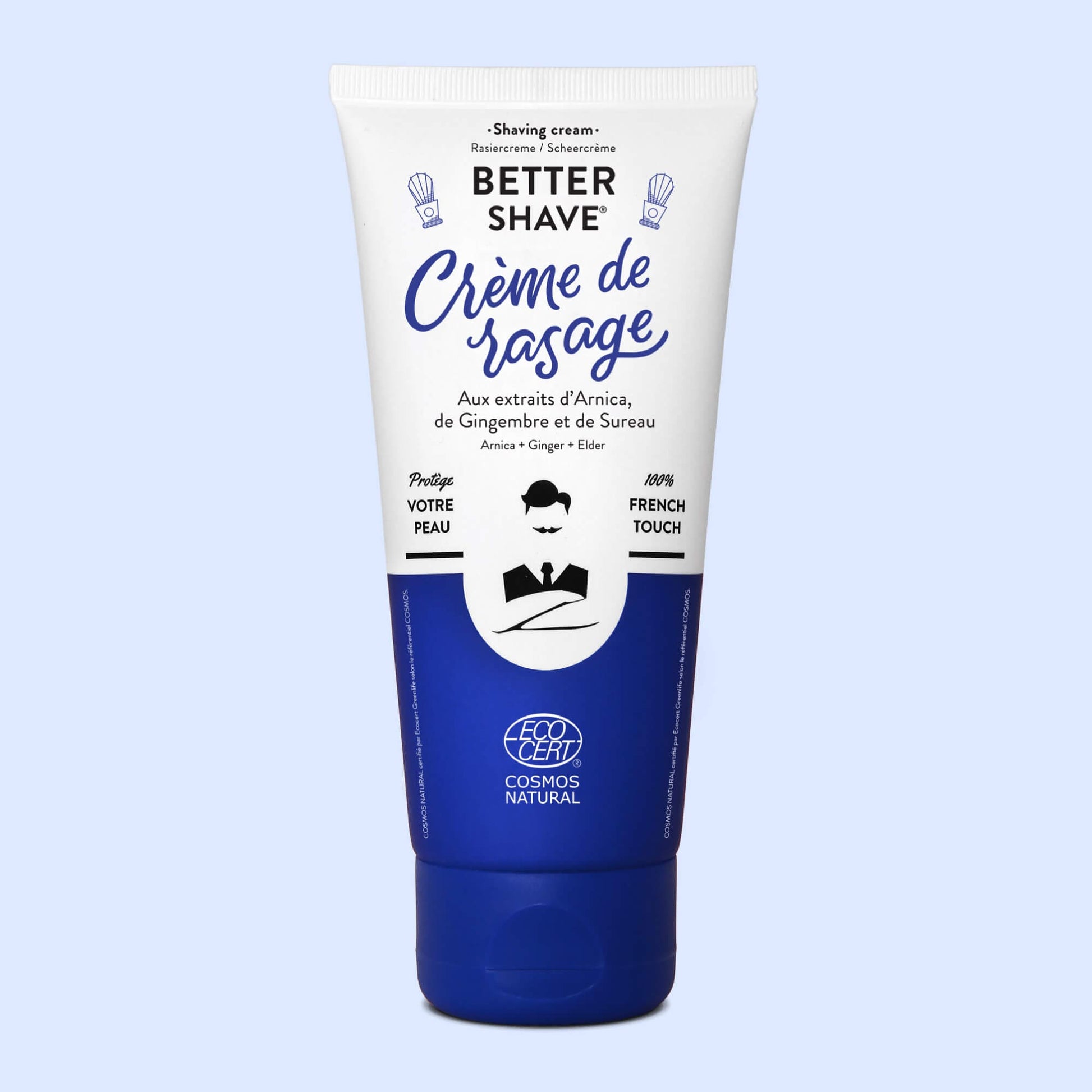 Tube de crème de rasage Monsieur BARBIER BETTER SHAVE avec design épuré, affichant des extraits d'Arnica, de Cyprès et de Gingembre, étiquette bleue et blanche, certifié Eco Cert Cosmos Natural, devant un fond neutre.