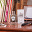 Flacon de parfum Monsieur BARBIER AMBRE & Lumière 100 ml posé près de son étui blanc sur un bureau en bois, notes de bergamote et ambre, ambiance vintage avec livres et rasoir.