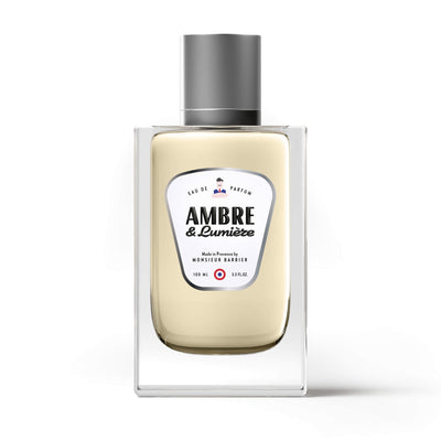 Flacon du parfum Monsieur BARBIER AMBRE & LUMIÈRE 100 ml en vue de face, étiquette blanche et noire sur fond clair, ambiance minimaliste.