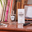 Flacon de parfum Monsieur BARBIER SANTAL Cruise 100 ml posé près de son étui blanc sur un bureau en bois, notes de mandarine et santal, ambiance vintage avec livres et rasoir.