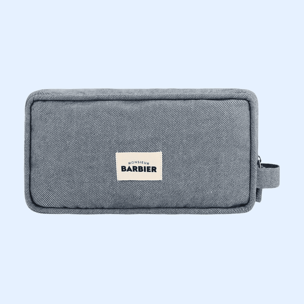 Blue denim toiletry bag from the brand 'Monsieur Barbier' with a visible label on the front displaying the brand name.