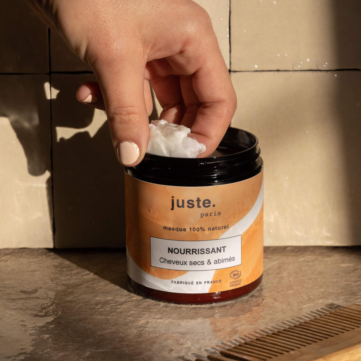 Pot du masque nourrissant cheveux secs et abîmés juste. paris, main prélevant une noisette de masque